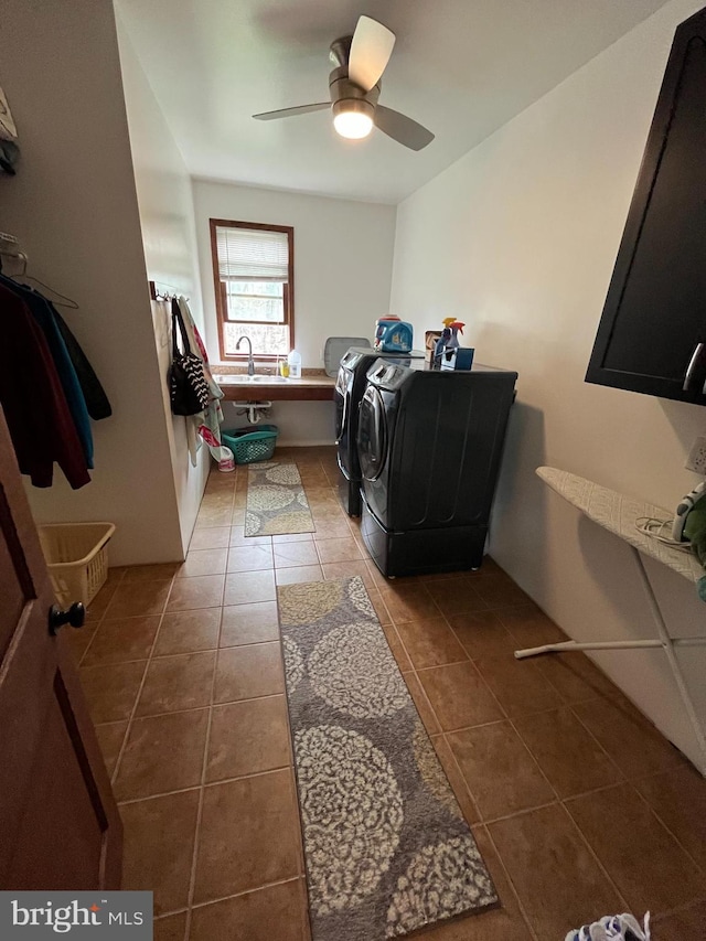 clothes washing area featuring washing machine and clothes dryer, a ceiling fan, a sink, cabinet space, and dark tile patterned floors