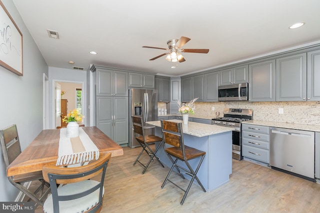 kitchen featuring visible vents, a center island, tasteful backsplash, gray cabinetry, and stainless steel appliances