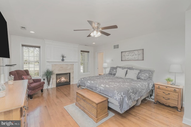 bedroom with a fireplace, a ceiling fan, light wood-type flooring, and visible vents