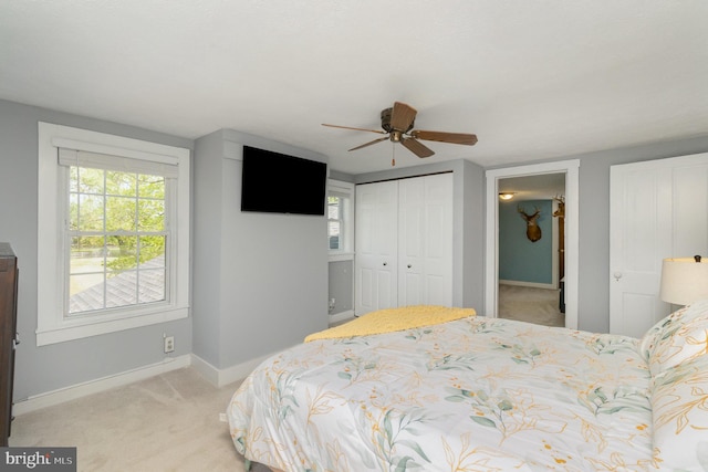 bedroom featuring baseboards, ceiling fan, a closet, and light colored carpet