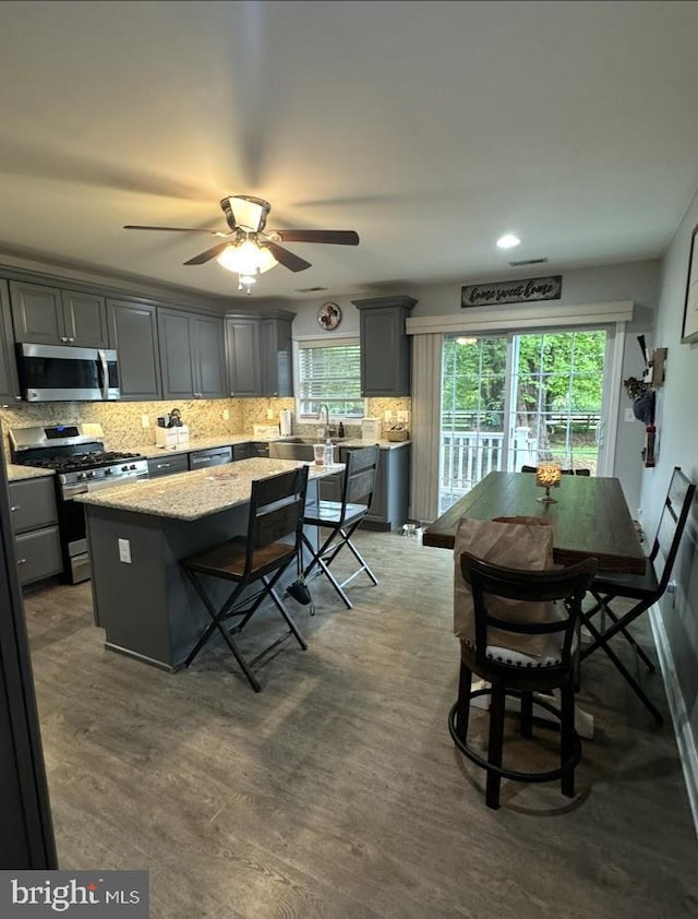 kitchen featuring a kitchen island, appliances with stainless steel finishes, backsplash, and a healthy amount of sunlight
