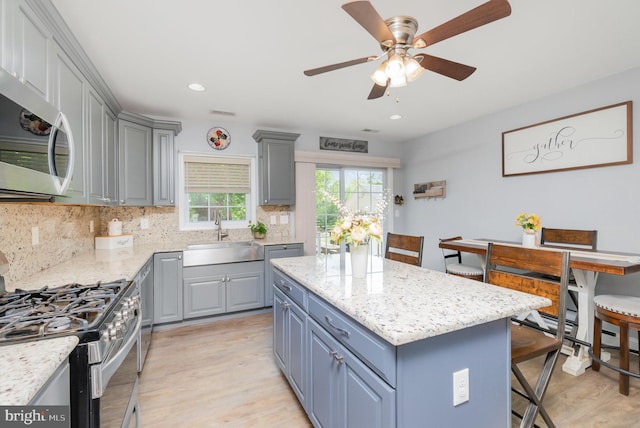 kitchen featuring gray cabinets, decorative backsplash, a center island, a sink, and stainless steel appliances