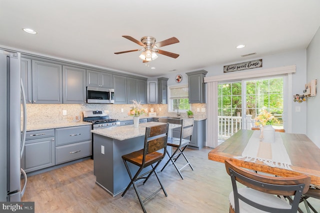 kitchen with appliances with stainless steel finishes, gray cabinets, a ceiling fan, and light wood finished floors