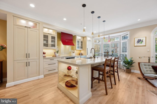 kitchen featuring light wood finished floors, open shelves, a sink, crown molding, and a kitchen island with sink