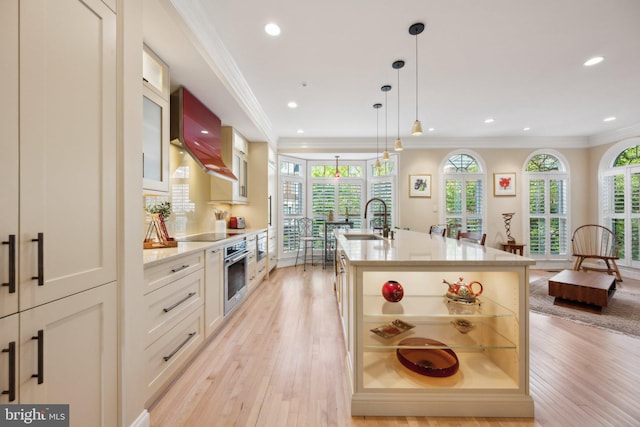 kitchen featuring stainless steel oven, wall chimney exhaust hood, a sink, and light wood-type flooring