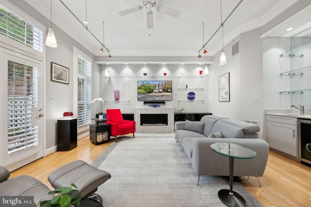 living room featuring a ceiling fan, light wood finished floors, a fireplace, ornamental molding, and visible vents