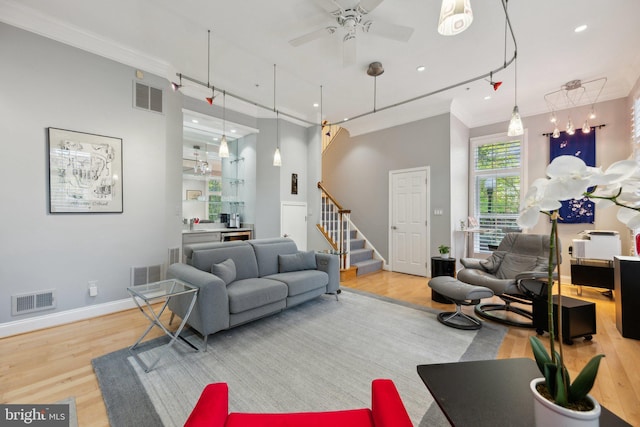 living area with wood finished floors, visible vents, crown molding, and stairs