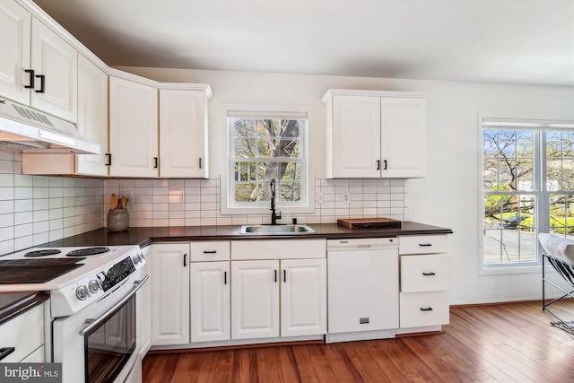 kitchen featuring a sink, dark countertops, under cabinet range hood, and white appliances