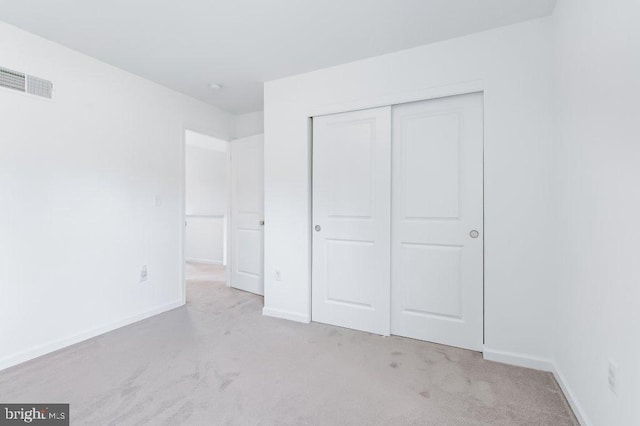 unfurnished bedroom featuring visible vents, a closet, baseboards, and light carpet