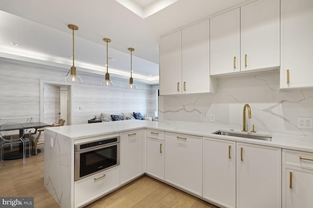 kitchen featuring a peninsula, stainless steel oven, white cabinetry, a sink, and backsplash