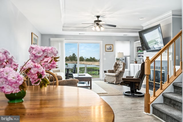dining room with ceiling fan, stairs, wood finished floors, a tray ceiling, and ornamental molding