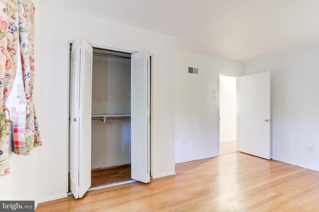 unfurnished bedroom featuring visible vents, wood finished floors, and a closet