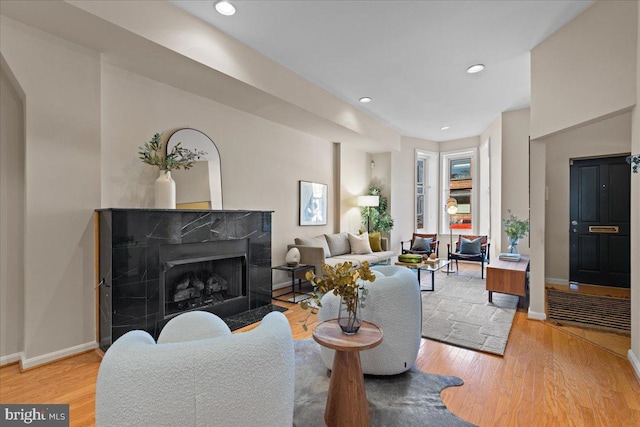 living room with a high end fireplace, light wood finished floors, baseboards, and recessed lighting