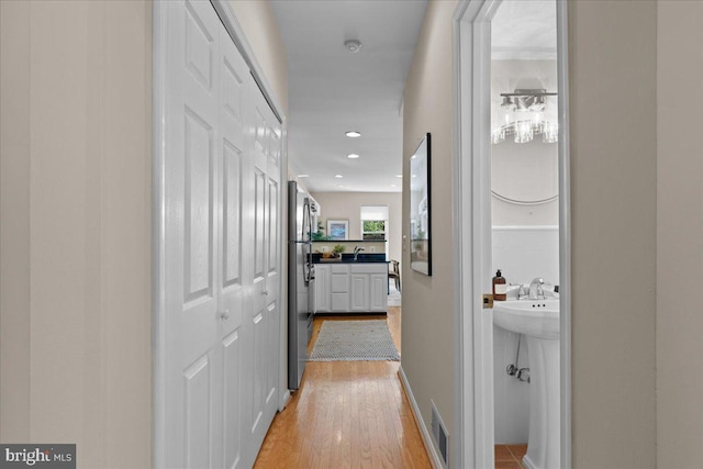 hallway with recessed lighting, visible vents, light wood finished floors, and a sink