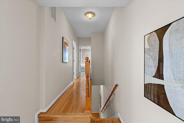 hall featuring visible vents, baseboards, wood finished floors, and an upstairs landing