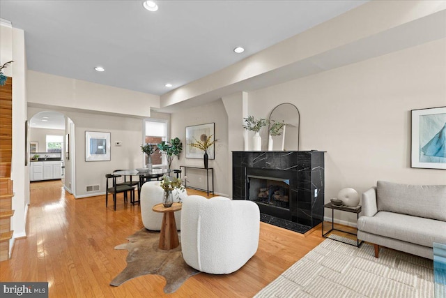 living area featuring light wood finished floors, arched walkways, visible vents, recessed lighting, and a premium fireplace