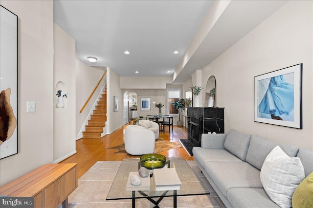 living room featuring light wood-style flooring, arched walkways, baseboards, recessed lighting, and stairs