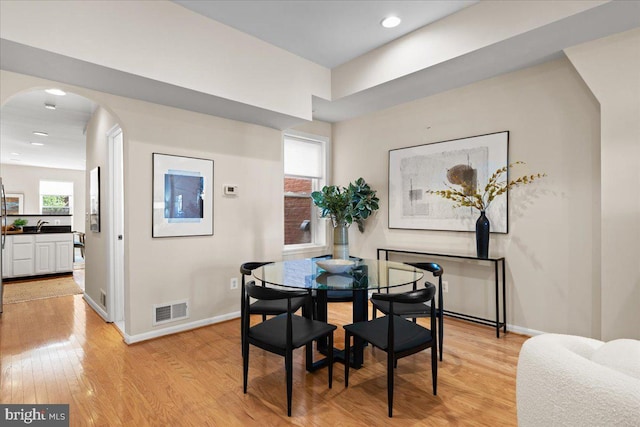 dining room with light wood-style floors, arched walkways, visible vents, and baseboards