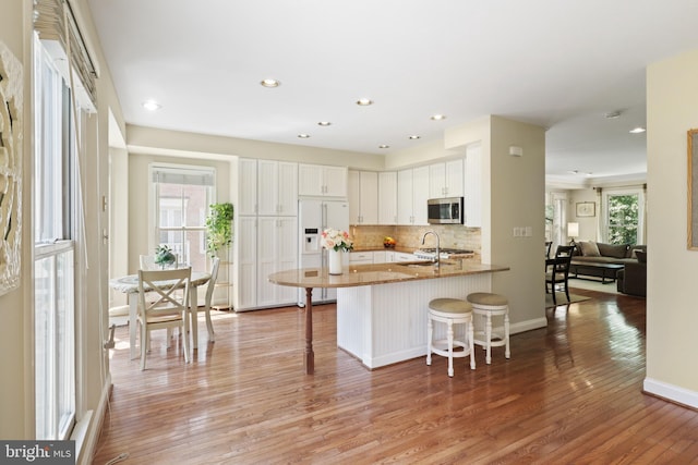 kitchen with white refrigerator with ice dispenser, a kitchen bar, stainless steel microwave, tasteful backsplash, and light wood-style flooring
