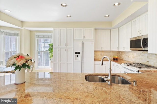 kitchen featuring a sink, recessed lighting, light stone countertops, and white appliances