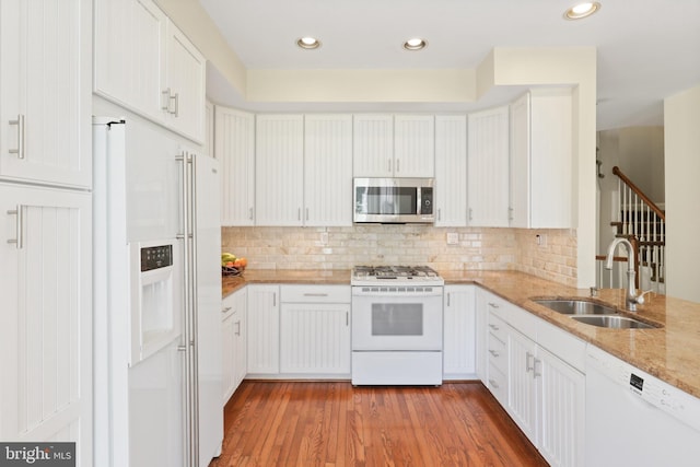 kitchen featuring white appliances, white cabinets, tasteful backsplash, light stone counters, and a sink