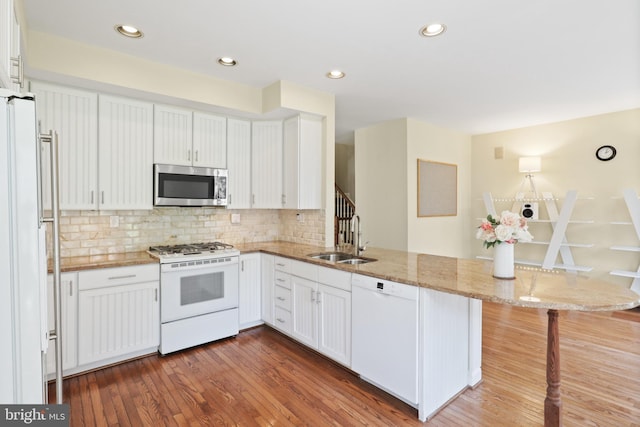 kitchen featuring light stone countertops, wood finished floors, a sink, a peninsula, and white appliances
