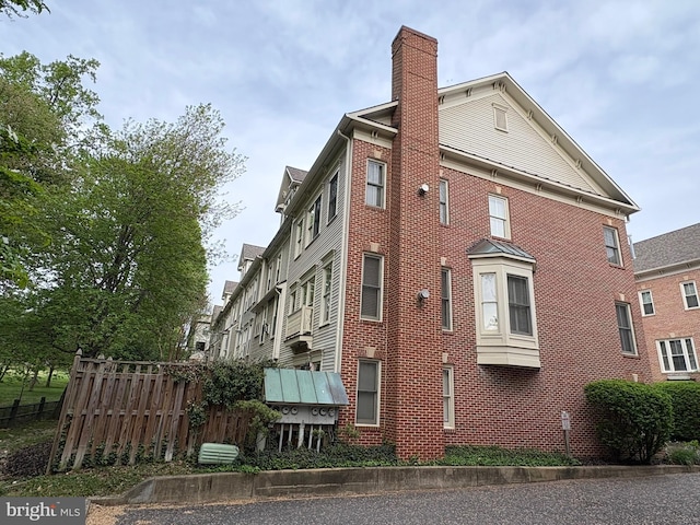 view of property exterior featuring brick siding, fence, and a chimney