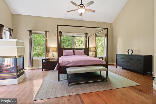 bedroom featuring a multi sided fireplace, baseboards, vaulted ceiling, and wood finished floors