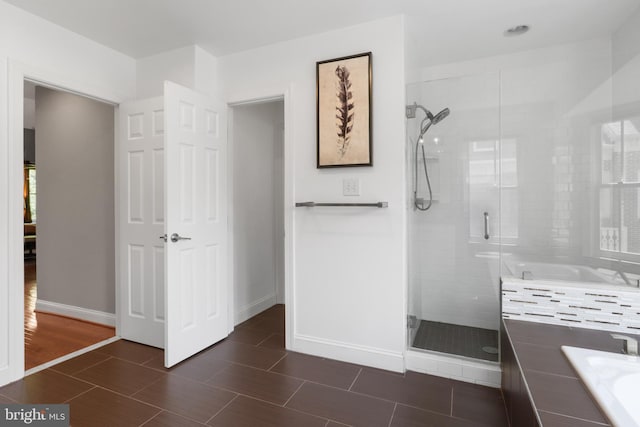 bathroom with baseboards, a stall shower, a bath, and wood finish floors