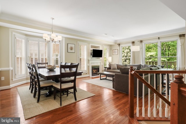 dining space with crown molding, a lit fireplace, hardwood / wood-style floors, and a notable chandelier