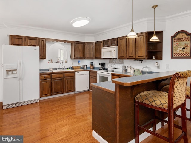 kitchen featuring white appliances, decorative light fixtures, a sink, a peninsula, and a kitchen breakfast bar