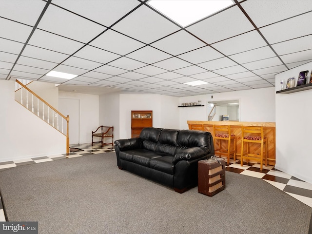 living area featuring tile patterned floors, a drop ceiling, stairs, and a dry bar