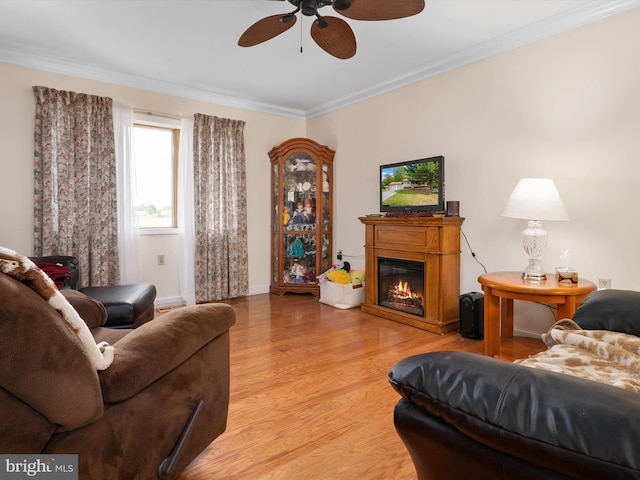 living room with crown molding, light wood-style flooring, ceiling fan, baseboards, and a glass covered fireplace
