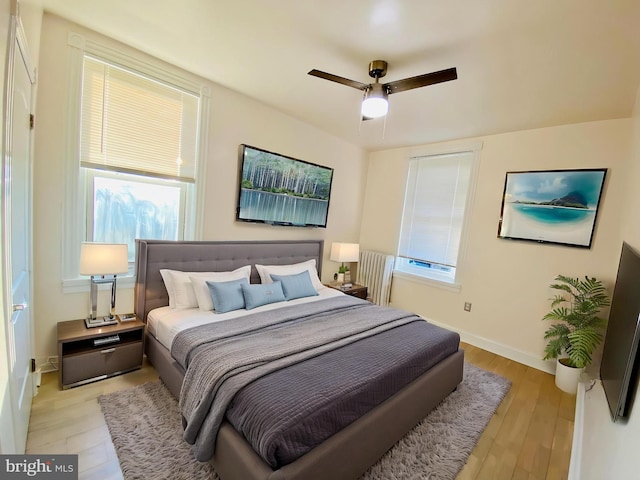 bedroom featuring a ceiling fan, baseboards, light wood-style floors, and multiple windows
