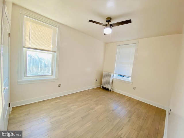 empty room with radiator, baseboards, ceiling fan, and light wood-type flooring