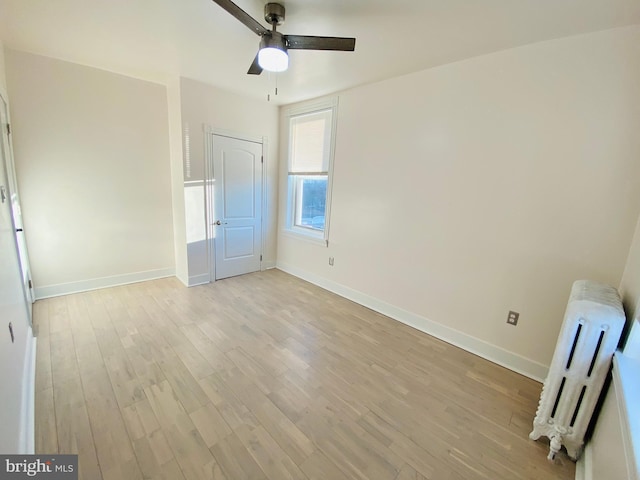 unfurnished bedroom featuring ceiling fan, baseboards, radiator heating unit, and light wood-style flooring