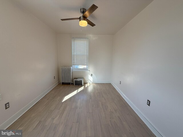 spare room with wood finished floors, baseboards, ceiling fan, and radiator