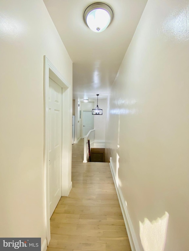 hallway featuring light wood-type flooring, baseboards, and an upstairs landing
