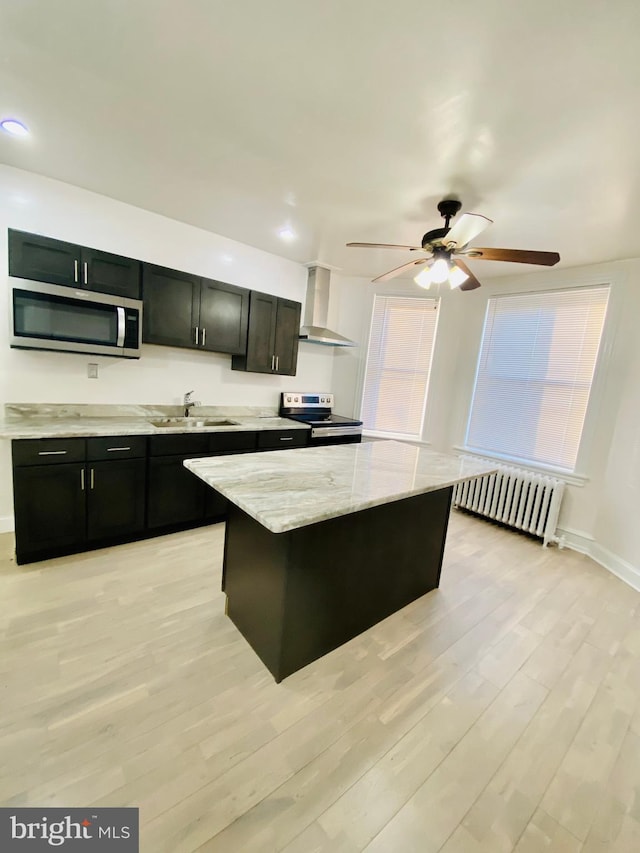 kitchen featuring stainless steel appliances, a sink, radiator heating unit, wall chimney range hood, and dark cabinets