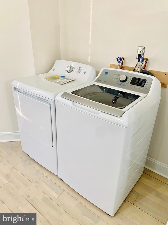 clothes washing area with laundry area, light wood finished floors, baseboards, and separate washer and dryer