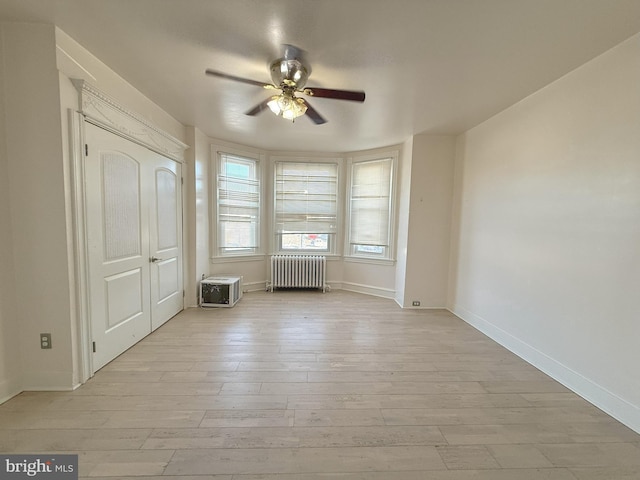 unfurnished bedroom featuring baseboards, light wood-style floors, ceiling fan, and radiator
