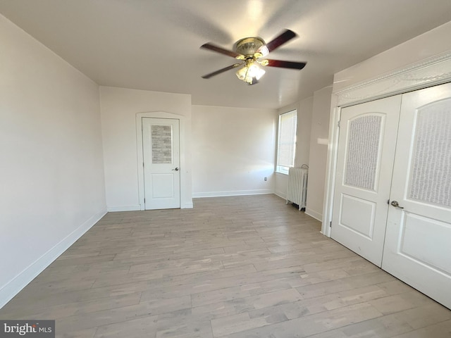 unfurnished bedroom featuring light wood finished floors, baseboards, ceiling fan, and radiator