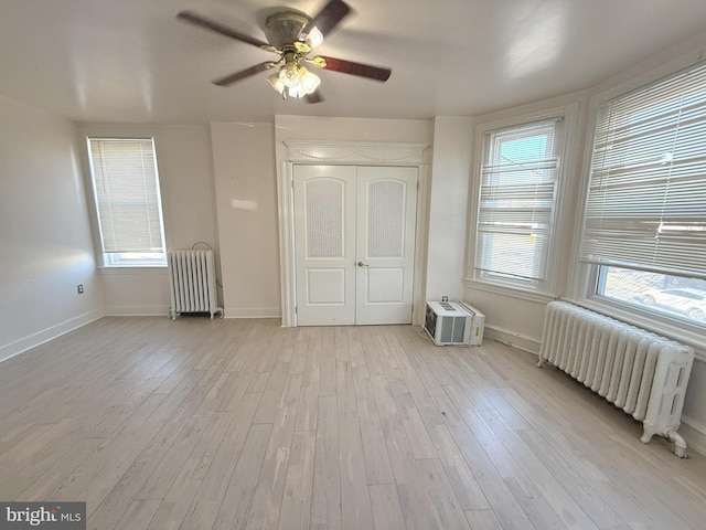 unfurnished bedroom with light wood-style flooring, baseboards, a wall unit AC, and radiator