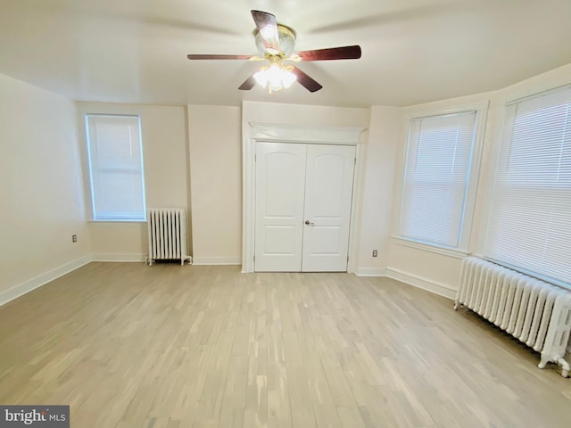 unfurnished bedroom featuring radiator, light wood-type flooring, a closet, and baseboards
