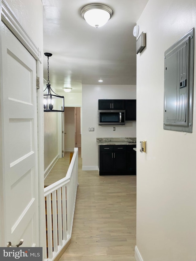 corridor with a notable chandelier, electric panel, baseboards, and light wood-style floors
