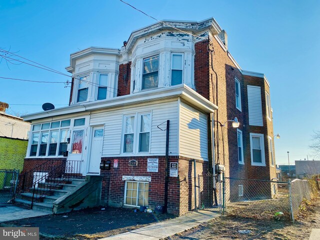 view of front facade with a gate, brick siding, fence, and entry steps