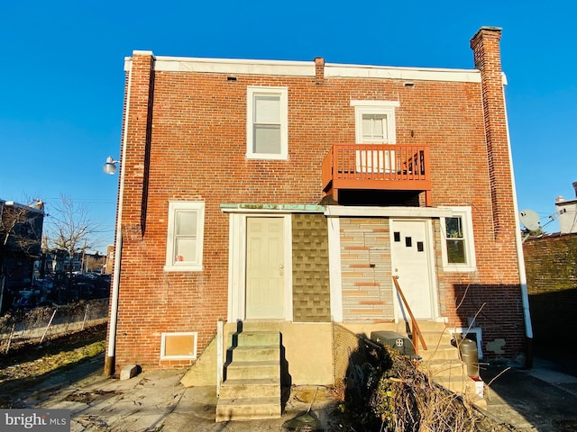 back of house with entry steps, brick siding, and a balcony