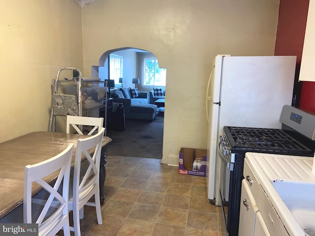 919 Dudley St, Philadelphia, PA 19148 - kitchen featuring stainless steel range with gas stovetop, arched walkways, dark carpet, freestanding refrigerator, and dark stone finish floors