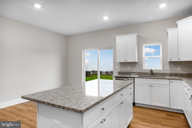 kitchen featuring plenty of natural light, light stone countertops, a center island, and a sink