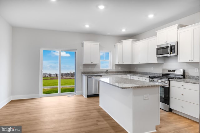 kitchen with a center island, a sink, light wood-type flooring, white cabinetry, and appliances with stainless steel finishes